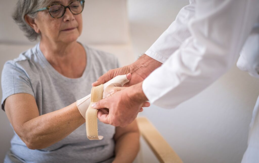 Doctor places bandage on the wrist of a senior female patient